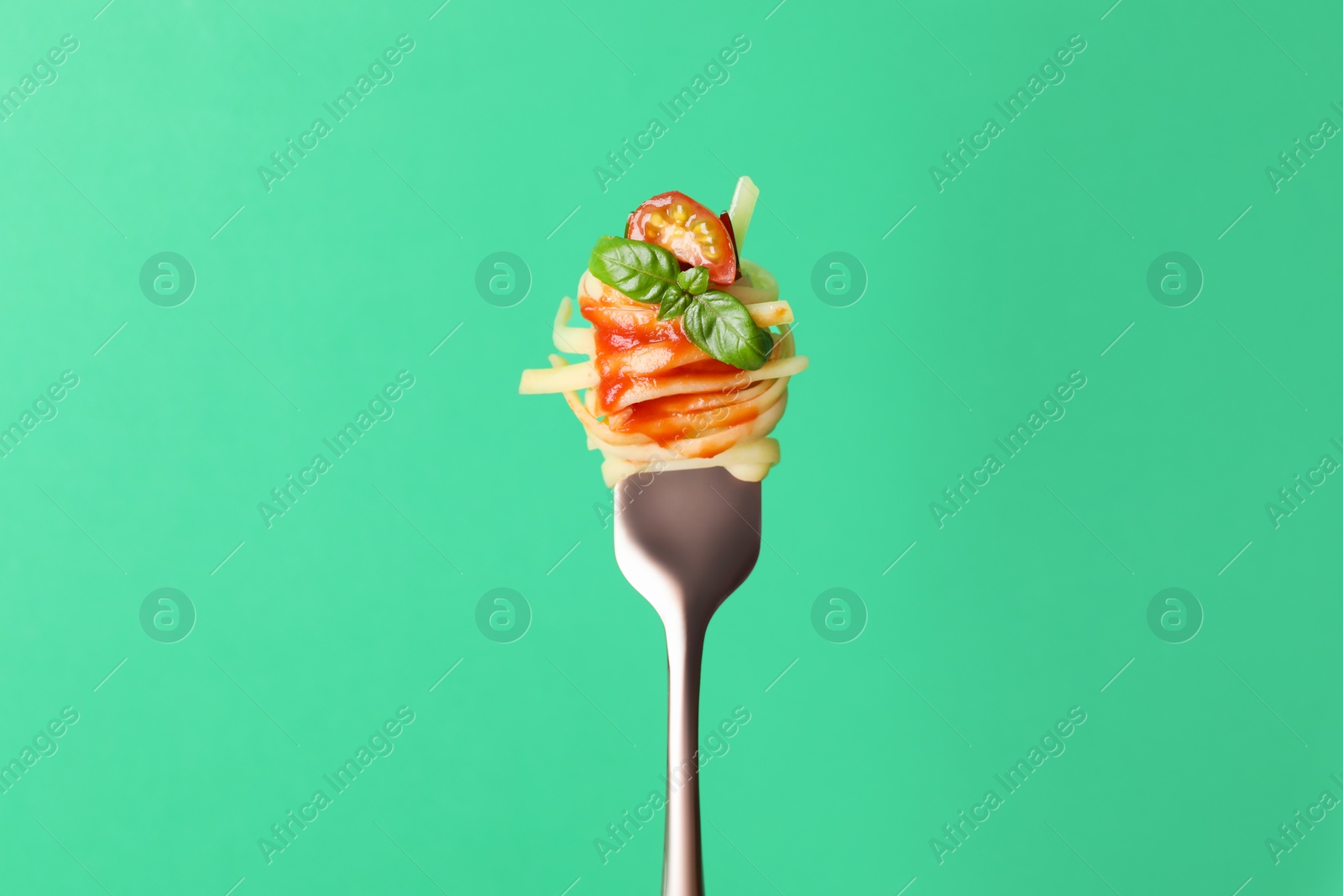 Photo of Tasty pasta with tomato sauce and basil on fork against green background