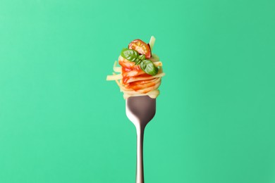 Tasty pasta with tomato sauce and basil on fork against green background