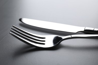 Photo of Shiny fork and knife on grey table, closeup