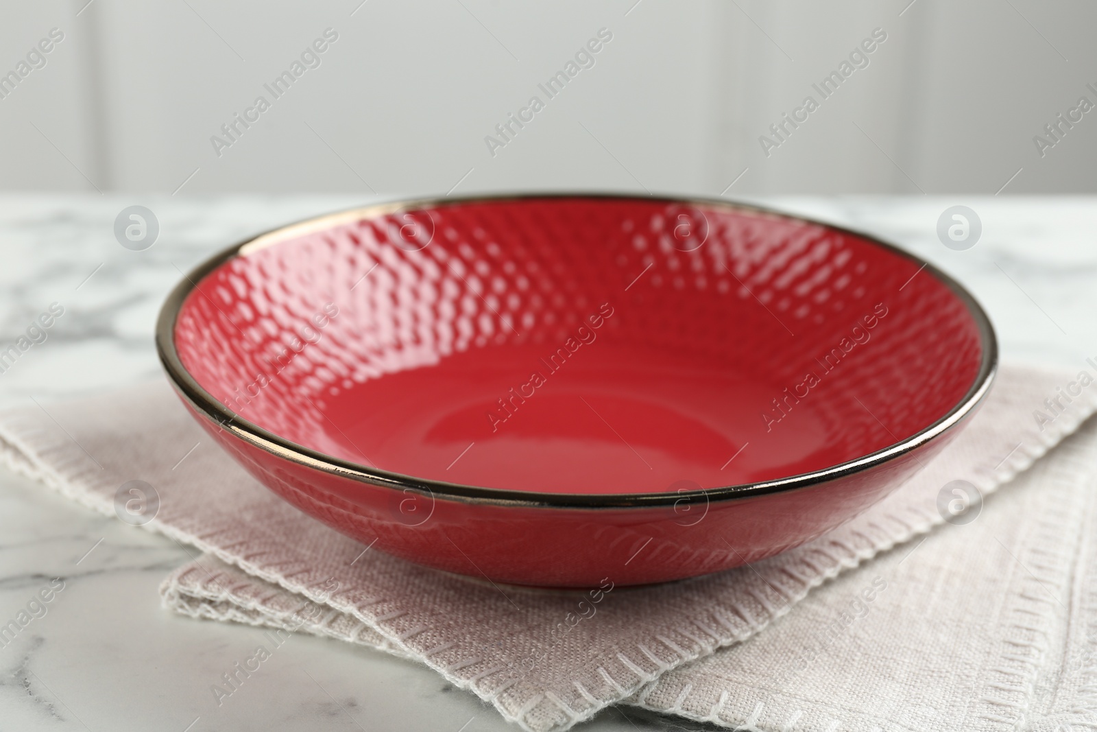 Photo of Beautiful red ceramic bowl and napkin on table, closeup