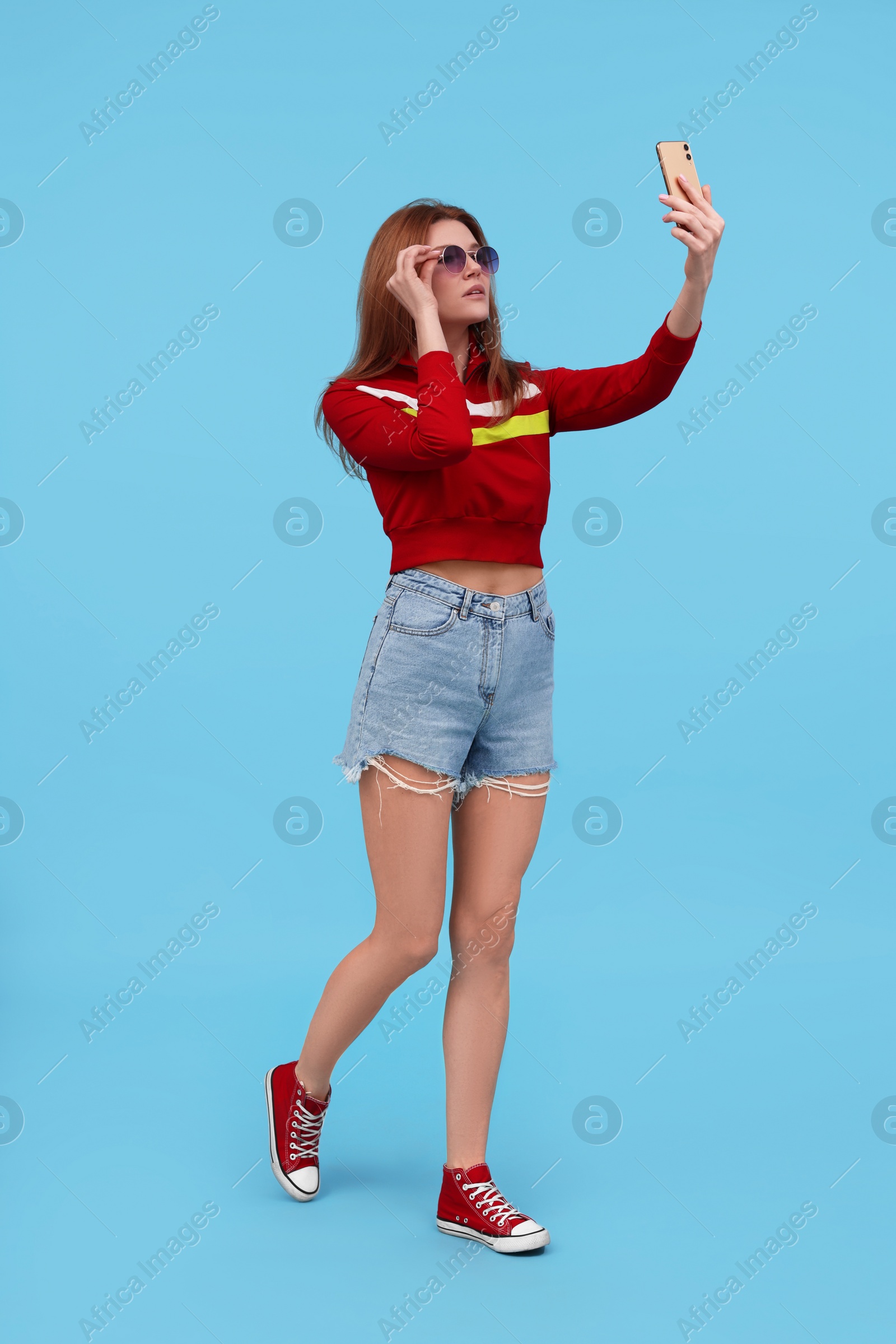 Photo of Beautiful woman in sunglasses taking selfie on light blue background