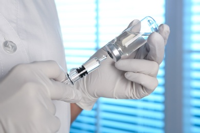Photo of Doctor filling syringe with vaccine from vial indoors, closeup