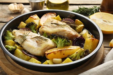 Photo of Pieces of delicious baked cod with vegetables, lemon and spices in dish on table, closeup