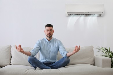 Image of Man resting under air conditioner on white wall at home