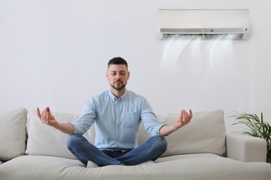 Man resting under air conditioner on white wall at home