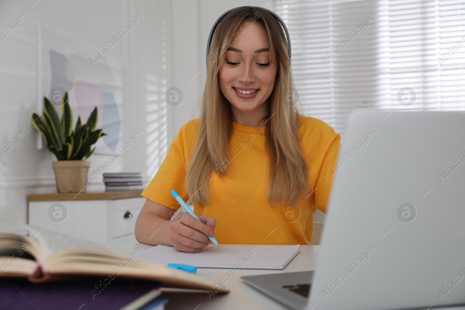 Photo of Young woman writing down notes during webinar at table in room