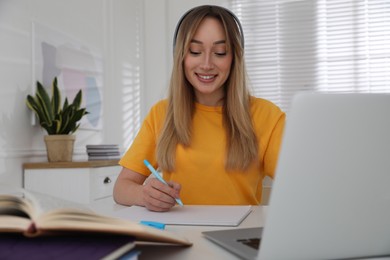 Young woman writing down notes during webinar at table in room