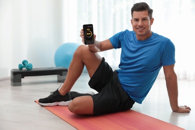 Photo of Man showing smartphone with fitness app indoors