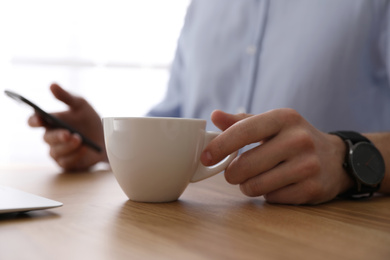 Man with cup of coffee at table indoors, closeup