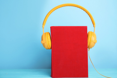 Photo of Book and modern headphones on light blue wooden table