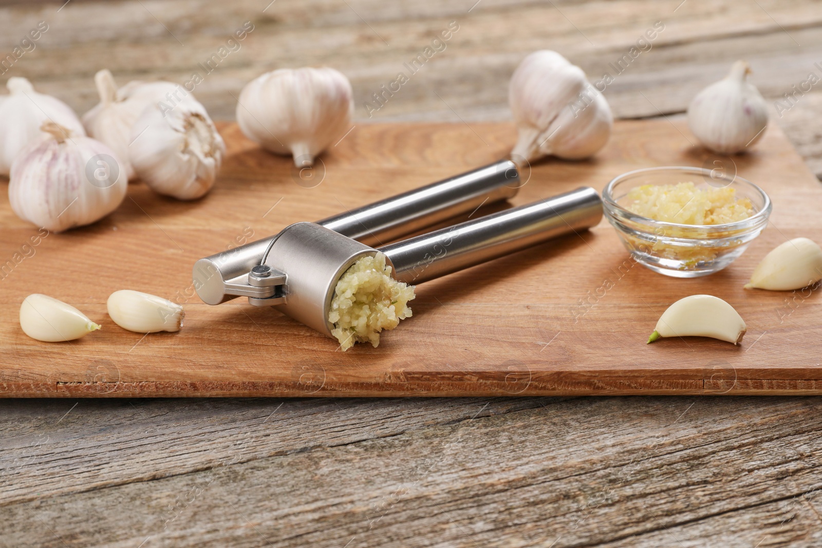 Photo of Garlic press, cloves and mince on wooden table. Kitchen utensil