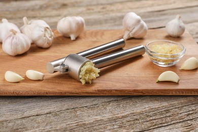 Photo of Garlic press, cloves and mince on wooden table. Kitchen utensil