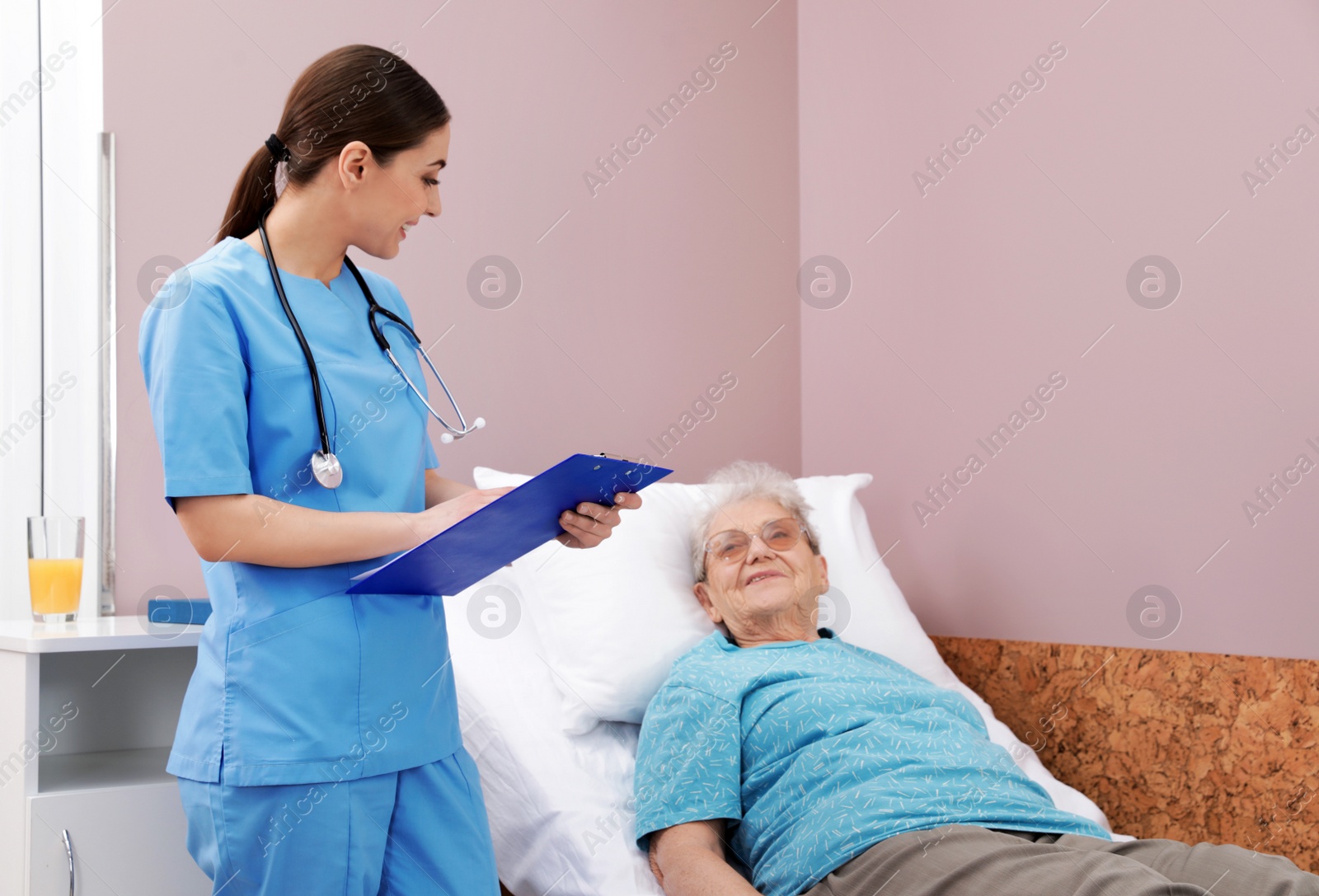 Photo of Nurse assisting senior woman lying on bed in hospital ward