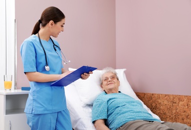 Nurse assisting senior woman lying on bed in hospital ward