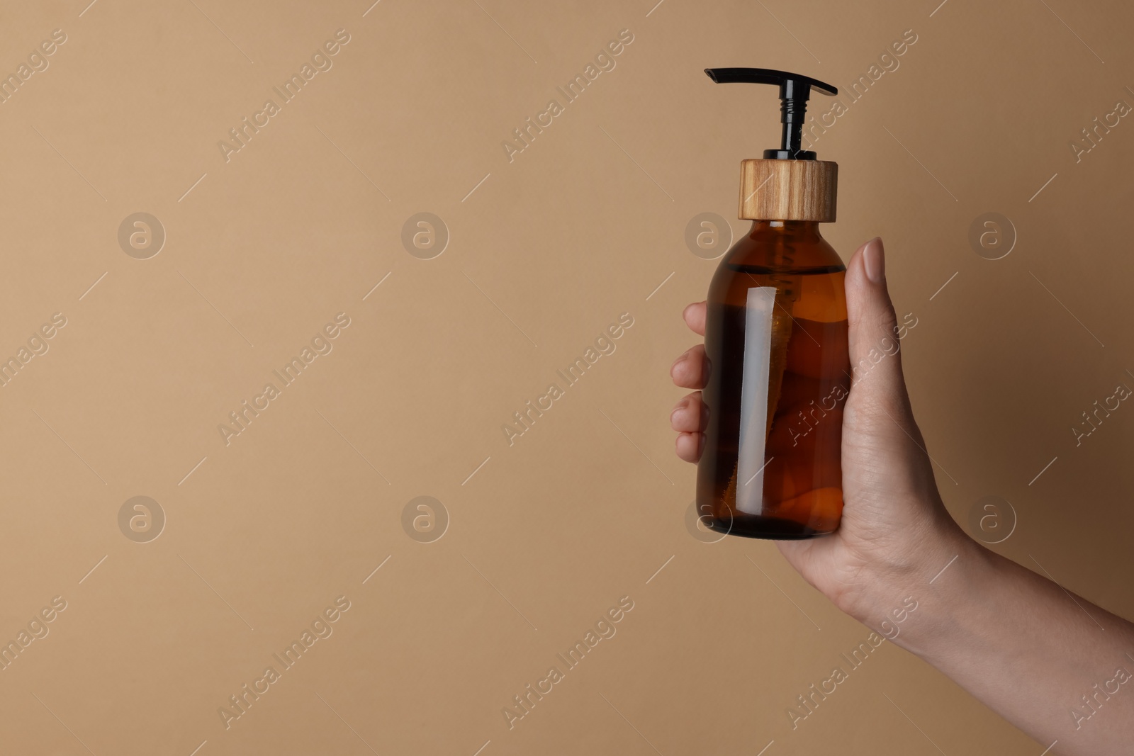 Photo of Woman holding bottle of cosmetic product on beige background, closeup. Space for text