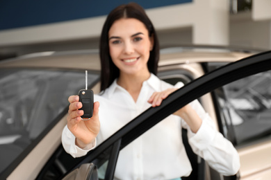 Saleswoman with key near car in dealership, focus on hand