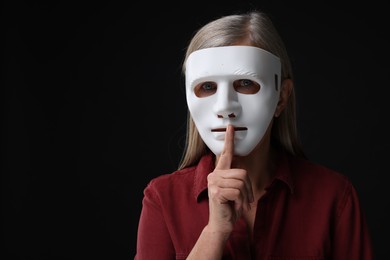 Multiple personality concept. Woman in mask showing hush gesture on black background, space for text