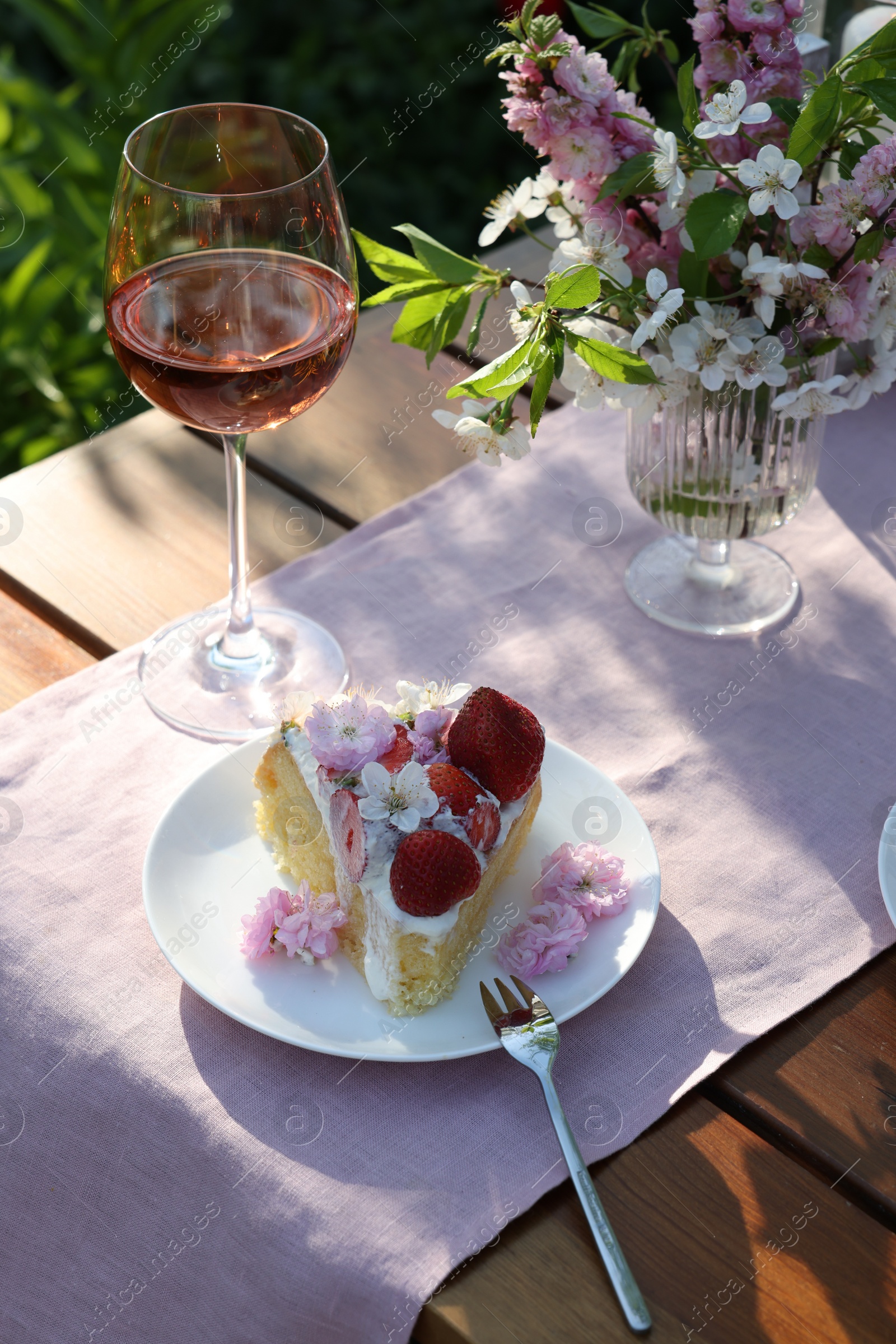 Photo of Vase with spring flowers, wine and cake on table served for romantic date in garden