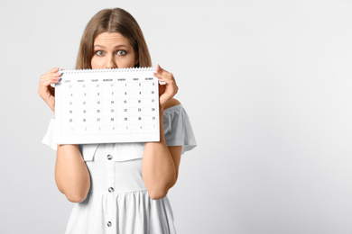 Photo of Young woman holding calendar with marked menstrual cycle days on light background. Space for text