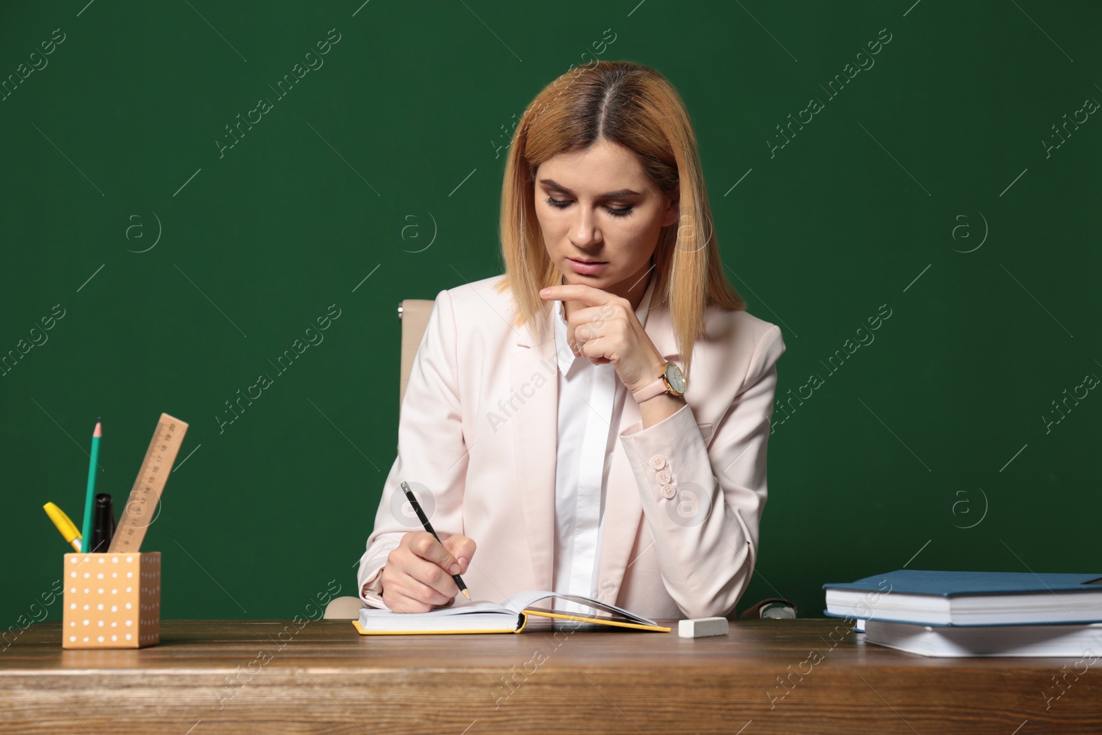 Photo of Portrait of beautiful teacher sitting at table near chalkboard