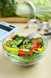 Photo of Calculator, tasty salad in bowl and other food on wooden table. Weight loss concept