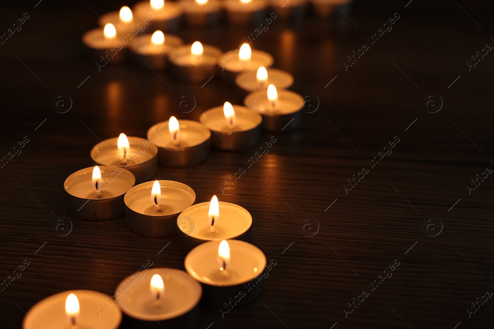 Photo of Burning candles on wooden table in darkness, space for text