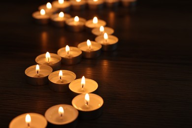 Photo of Burning candles on wooden table in darkness, space for text