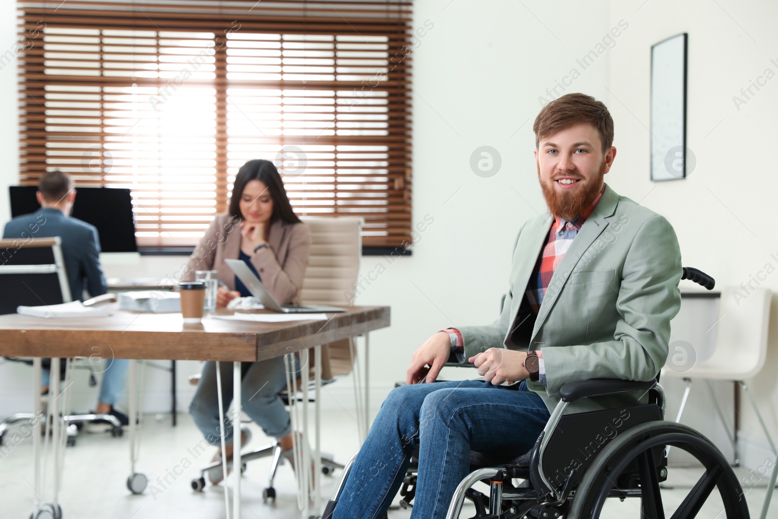 Photo of Young man in wheelchair with colleagues at office