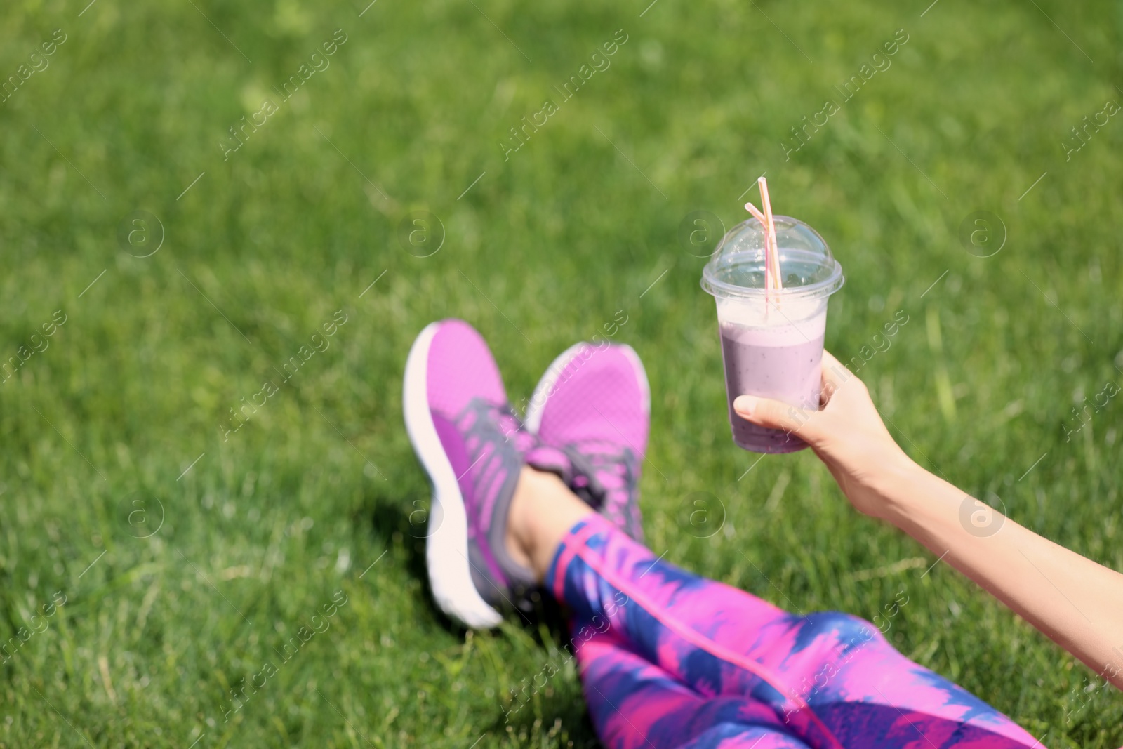 Photo of Young woman in sportswear with plastic cup of healthy smoothie on grass outdoors