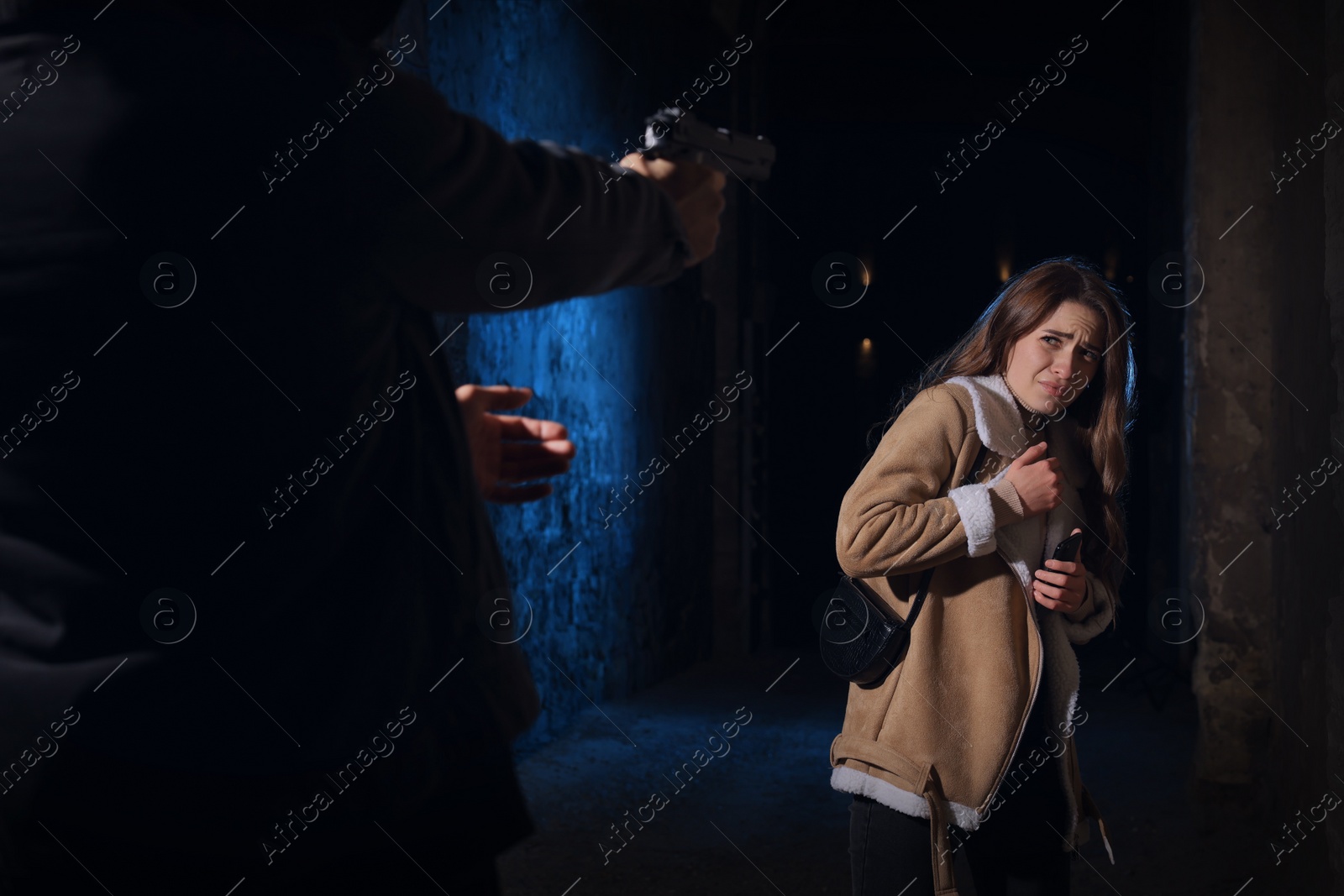 Photo of Criminal threatening young woman with gun in alley at night. Self defense concept