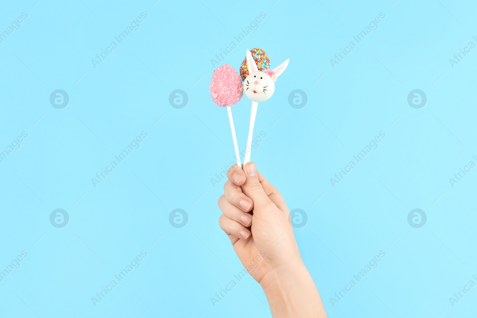 Photo of Woman with delicious cake pops on light blue background, closeup. Easter holiday