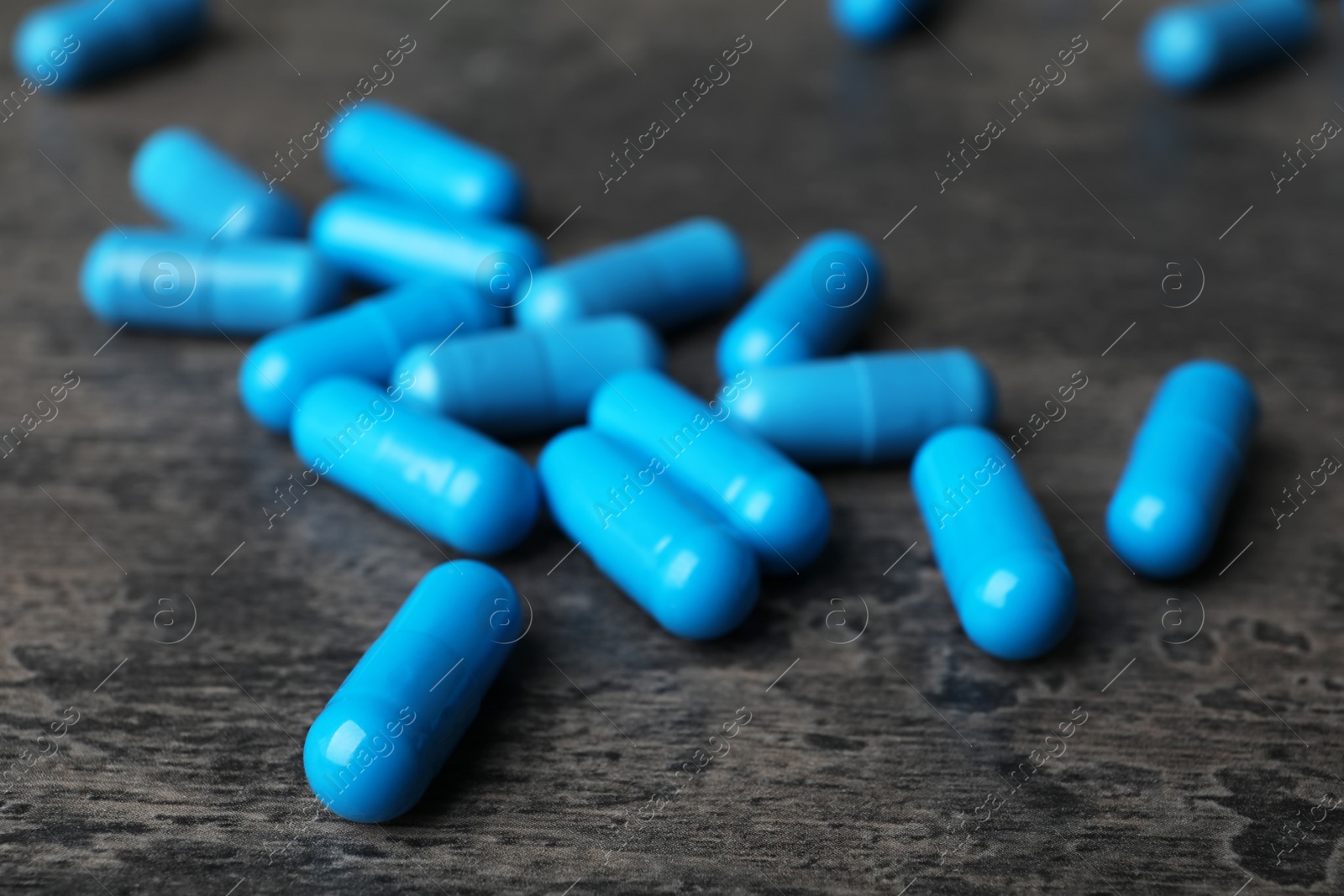 Photo of Many blue pills on dark surface, closeup