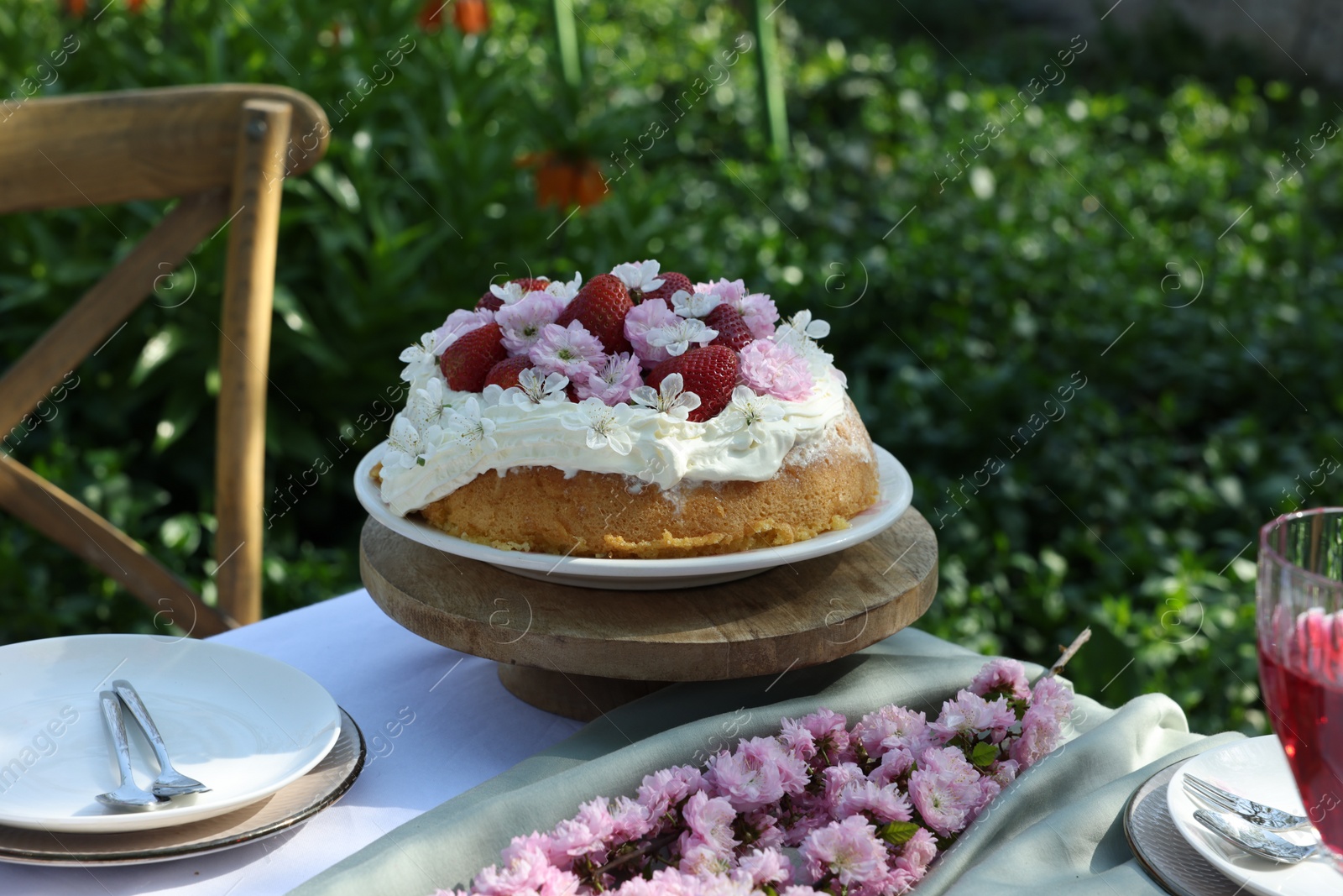 Photo of Beautiful spring flowers and delicious cake on table in garden