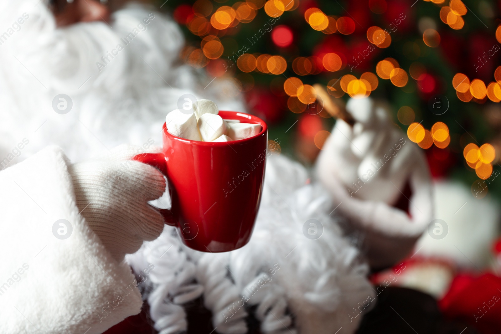 Photo of Santa Claus with hot drink and cookie against blurred Christmas lights, closeup