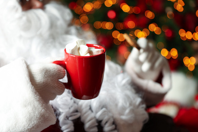 Santa Claus with hot drink and cookie against blurred Christmas lights, closeup