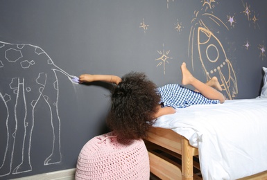 African-American child drawing with chalk on wall in bedroom