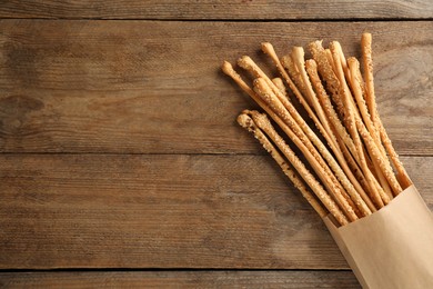 Delicious grissini sticks in paper bag on wooden table, top view. Space for text