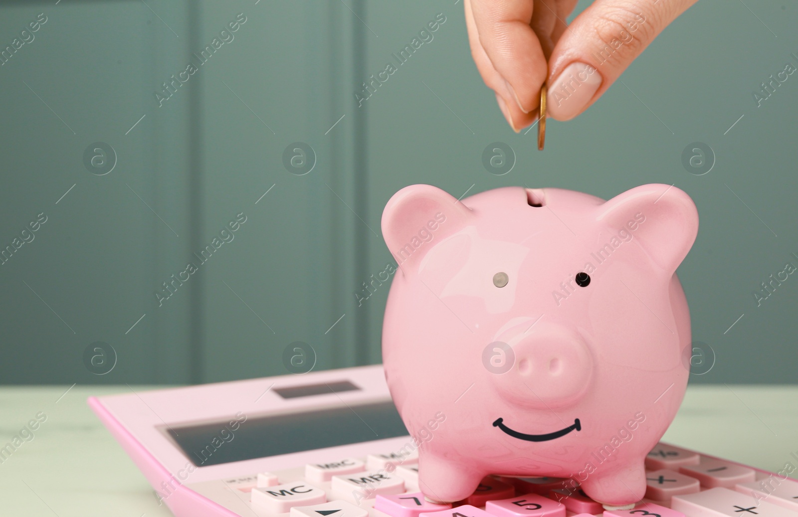 Photo of Woman putting coin into piggy bank at white table, closeup. Space for text