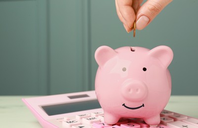 Woman putting coin into piggy bank at white table, closeup. Space for text