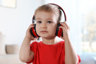 Photo of Cute child listening to music with headphones indoors