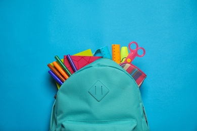Stylish backpack with different school stationary on blue background, top view
