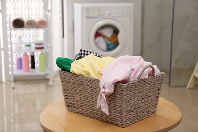 Wicker laundry basket full of different clothes on table in bathroom