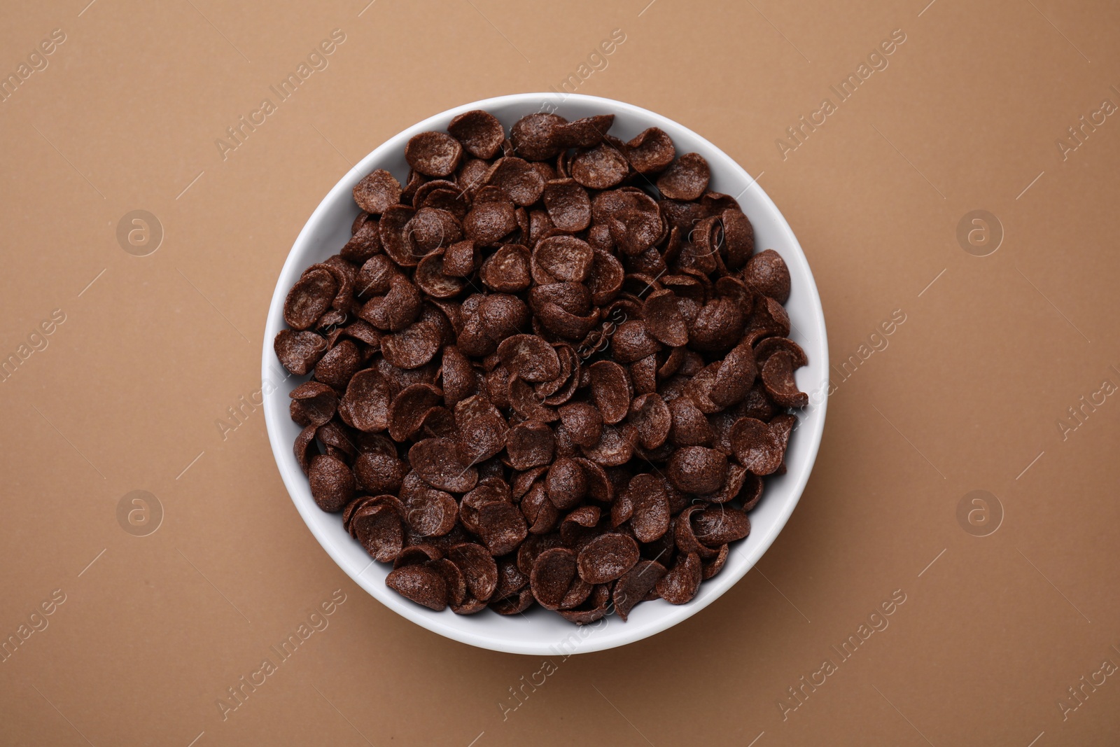 Photo of Breakfast cereal. Chocolate corn flakes in bowl on brown table, top view