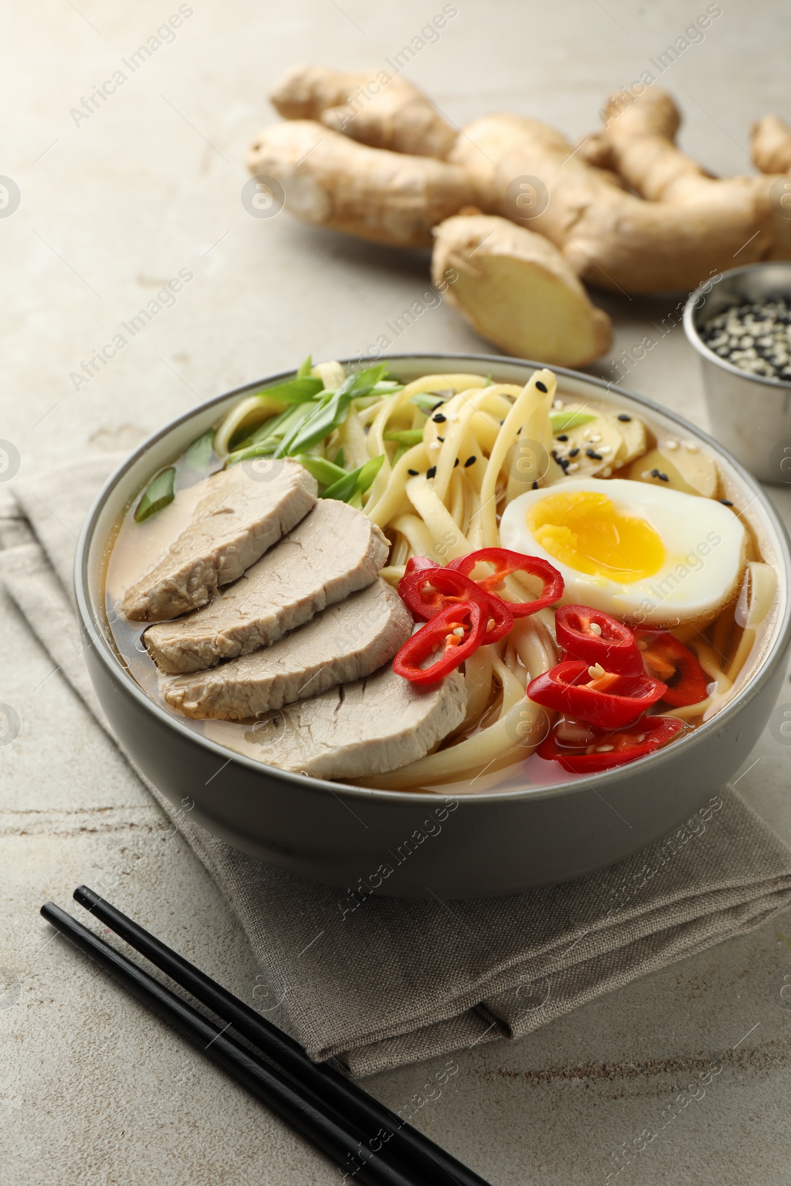 Photo of Delicious ramen in bowl and chopsticks on light textured table, closeup. Noodle soup