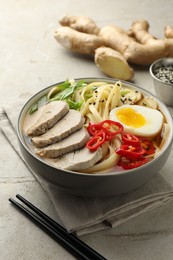 Delicious ramen in bowl and chopsticks on light textured table, closeup. Noodle soup