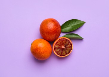 Photo of Ripe sicilian oranges and leaves on violet background, flat lay