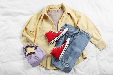 Pair of stylish red sneakers, clothes and bag on white fabric, flat lay