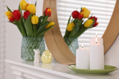 Photo of Easter decorations. Bouquet of tulips in vase, burning candles and figures on fireplace at home