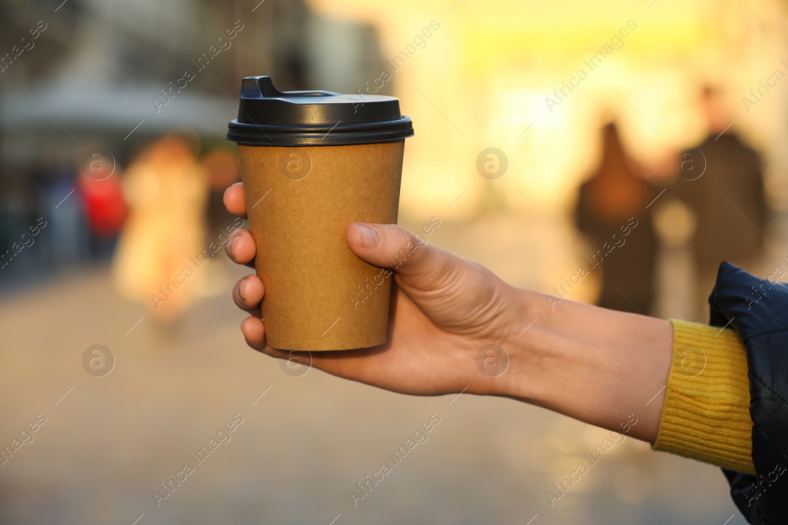 Photo of Woman holding paper takeaway cup on city street, closeup. Coffee to go