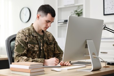 Photo of Military education. Young student in soldier uniform learning at wooden table in room